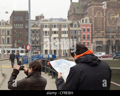 Tourist couple with woman taking digital photo and man looking at map, in Amsterdam, the Netherlands Stock Photo