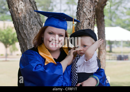 A young mother in graduation gown and cap posing with her small boy. The boy is wearing suspenders and cap. Stock Photo