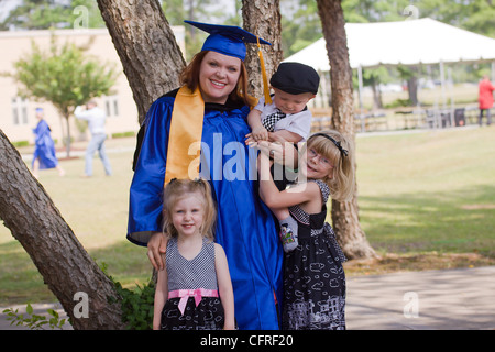 A young mother in graduation gown and cap posing with her family. The boy is wearing suspenders and cap and tie. Stock Photo