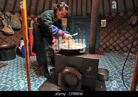 Mongolia, Baganuur District Inland, Pregnant Mongolian young woman wearing a traditional black winter coat and preparing food Stock Photo