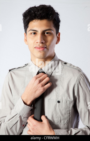 Handsome young Hispanic man  in a shirt and dark tie, looking   at the camera while adjusting his tie Stock Photo