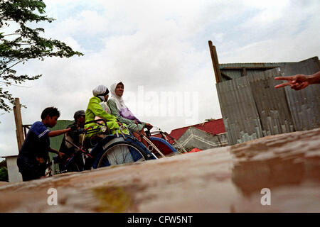 BEKASI, WEST JAVA, INDONESIA FEBRUARY 4, 2007:  Pedicab driver pushes his pedicab with two women passengers at the flooded street. Severe storm caused the flooding in Indonesia capital, as river broke their banks, inundating thousands of homes and business.  Photo by Edy Purnomo/JiwaFoto Stock Photo