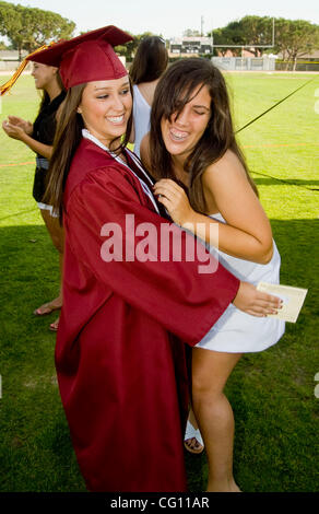 A happy graduating high school senior gets a congratulatory hug from a classmate during outdoor commencement exercises in Huntington Beach, CA. Stock Photo