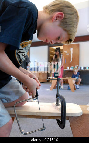 FREESTANDING--Eric Mortl, 8, blows off the sawdust as he cuts a guitar shape using a coping saw during the Kids' Carpentry class Tuesday, July 24, 2007, in Walnut Creek, Calif.  In the background Jeab Glass helps a student with a saw cut.  The class is offered through the Walnut Creek parks and recr Stock Photo