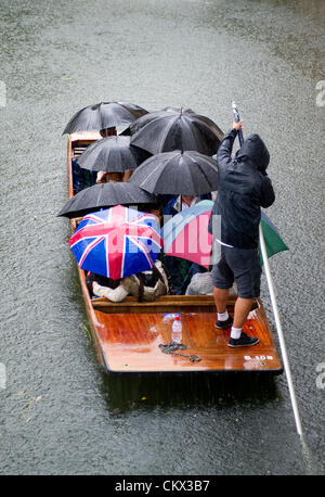 Cambridge, UK. Saturday 25th August 2012. Bank holiday weekend starts with a washout. Torrential rains and hail in Cambridge today. Visitors bring umbrellars on punt tours on the river Cam.