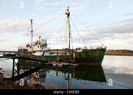 old fishing trawler named Hero with rusting green hull reflected in calm water of Willapa Bay on Pacific Coast of Washington State USA Stock Photo