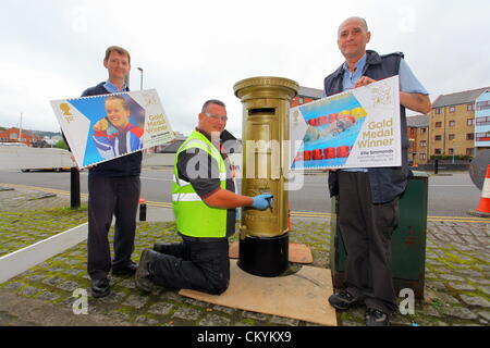 Swansea, UK. Tuesday 04 September 2012. Pictured: Streetwork supervisor Steve Vincent (C) painting a post box gold with local postmen Mark Richards (L) and Eban Davies (R)  holding the new stamps.    Re: A Royal Mail postbox has been painted gold in tribute to the second gold medal won by Paralympian swimmer Ellie Simmonds  in Trawler Road, in the Marina area of Swansea south Wales. Credit:  D Legakis / Alamy Live News Stock Photo