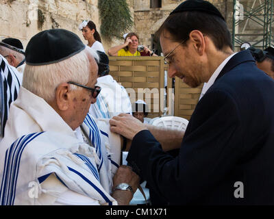 An elderly man is assisted in properly laying the tefilin, phylacteries, on his left arm at the Western Wall.  Jerusalem, Israel. 16-September-2012.  Thousands pray at the Western Wall on the Eve of the Jewish New Year for the last time in the year 5772. According to the Jewish calendar the year 5773 and the Jewish High Holidays will begin tonight after sunset. Stock Photo