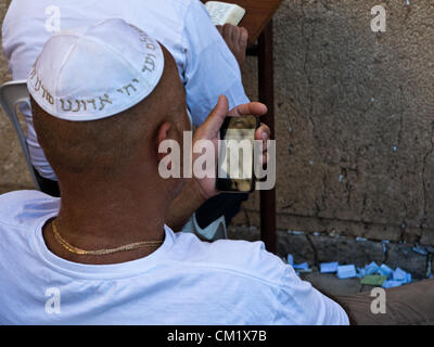 A man prays at the Western wall reading the prayers from an electronic prayer book on an iPhone. Jerusalem, Israel. 16-September-2012.  Thousands pray at the Western Wall on the Eve of the Jewish New Year for the last time in the year 5772. According to the Jewish calendar the year 5773 and the Jewish High Holidays will begin tonight after sunset. Stock Photo