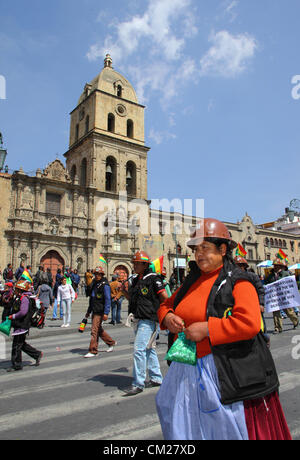 LA PAZ, BOLIVIA, 18th September 2012. Cooperative miners pass San Francisco church during a march to demand the government complies with promises to give them a greater share of the concession to the Colquiri mine near Oruro. Cooperative and salaried miners who work for the state mining company COMIBOL have been disputing control of the mine for several weeks, with protests escalating in the last week. The salaried miners are demanding the mine is nationalised and the cooperatives stopped from working there. The lady is carrying a bag of coca leaves to chew while marching. Stock Photo