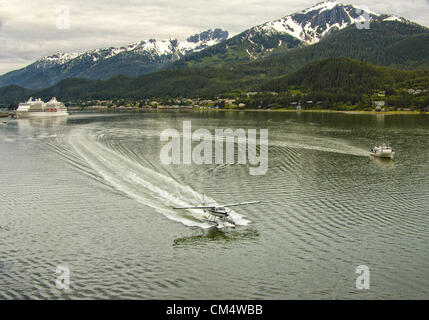 July 5, 2012 - Borough Of Juneau, Alaska, US - In the Gastineau Channel, returning to Juneau, a Wings Airways DeHavilland Otter flightseeing floatplane taxis after flying tourists over the Tongass National Forest and glaciers of the Juneau icefield. At right is the â€œCaptain Cook,â€ the Adventure Bound Alaska 65 ft trawler, after taking tourists on a glacier and fjord cruise. At left, the Regent Seven Seas Navigator, a luxury cruise ship, is docked on the Juneau side of the channel opposite mountainous, forested, Douglas Island. The tourism industry is a large contributor to the Alaskan econ Stock Photo