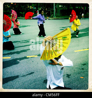 Oct. 7, 2012 - Bangkok, Thailand - Women do Tai Chi exercises with colorful fans in Lumphini Park in Bangkok. Lumphini Park is 142 acre (57.6-hectare) park in Bangkok, Thailand. This park offers rare open public space, trees and playgrounds in the congested Thai capital. It contains an artificial lake where visitors can rent boats. Exercise classes and exercise clubs meet in the park for early morning workouts and paths around the park totalling approximately 1.55 miles (2.5ÃŠkm) in length are a popular area for joggers. Cycling is only permitted during the day between the times of 5am to 3pm. Stock Photo