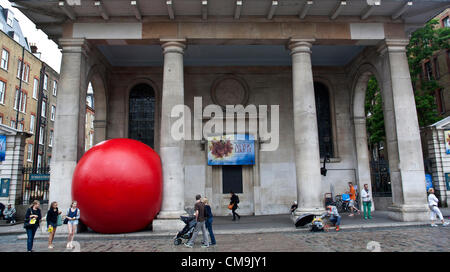 Covent Garden, London, UK. Friday 29th June 2012. The Big Red Ball Project arrives wedged between two pillars. Over the last three days it's appeared at the Golden Jubilee Bridge, Waterloo Bridge and now Covent garden. The artist, Kurt Perschke, has travelled the UK with the project from the south west towards London. It has been seen previously in Sydney, Taipei and Barcelona. Tomorrow it is on London's Southbank somewhere.