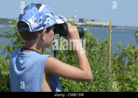 Young explorer. Niantic, Connecticut, USA, July 6, 2012 - From a high vantage point at McCooks Point Park, seven-year-old Nathanial 'Nate' Tirrell of Southbury, Connecticut wearing a blue military fatigue style cap looks out to sea with binoculars as some of the tall ships begin to appear in Niantic Bay in East Lyme during OpSail 2012 CT to spot tall ships, both military and civilian. The Millstone Nuclear Power Plant is in the distance. Model released.