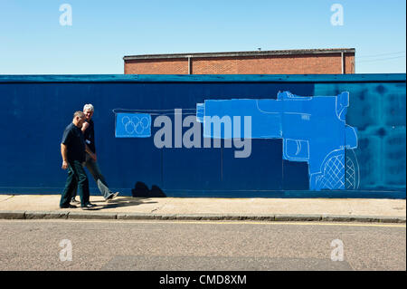 London, UK - 23 July 2012: Two men walk past a graffiti wall in Hackney Wick, close to the London 2012 Olympic Park. The area, once a major  manufacturing center in the UK, is now a mix of old warehouses converted into artist’s studio and industrial yards attracting now both tourists and Olympic staff members. Stock Photo