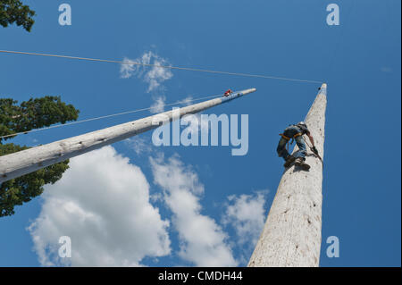 24th July 2012. Llanelwedd, Wales, UK. Contestants for the Welsh Open Speed Pole Climbing competition don a climbing harness and strap spiked trainers to their legs and feet to make a climbing assault on two perilous 100ft (30 metres approx) poles that rise up to the bright blue sky above from the Forestry Area at The Royal Welsh Showground where the 108th Royal Welsh Agricultural Show is taking place for four days this week at Llanelwedd in Mid Wales. Photo credit: Graham M. Lawrence/Alamy Live News Stock Photo