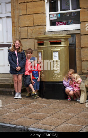 UK Monday 6 August 2012. Group of children posing by the Royal Mail gold painted post box at Sherborne, Dorset to recognise Olympic gold medalist Peter Wilson gold medal winner at Olympics London 2012 games. golden postbox  golden post box gold postbox gold post box gold mailbox golden mailbox gold letterbox golden letterbox gold mail box golden mail box. Stock Photo