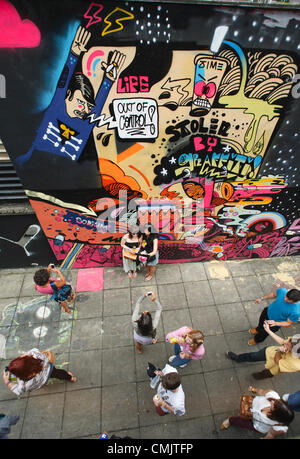 Bristol, UK. 18th August, 2012. Two women get their photograph taken in front of one of the artworks that have been painted on buildings in Nelson Street for the See No Evil street art festival. See No Evil is a collection of works of public art created by multiple graffiti and urban street artists which are located in and around Nelson Street in Bristol, UK. Stock Photo