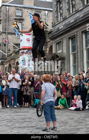 18 August 2012  Damien Ryan, an Australian street performer, riding a unicycle and juggling with fire torches in The Royal Mile, Edinburgh during the Edinburgh Fringe Festival. A small boy who had been helping him during his show, looks on. Stock Photo