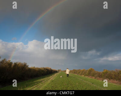 Over, Cambridgeshire, UK. 3rd Nov, 2013. A woman walks a dog under stormy Fen skies and a rainbow on the flood banks at Over in Cambridgeshire UK  3rd November 2013. It was a blustery but sunny day with occasional showers, dramatic under the wide open Fen skies. Credit Julian Eales/Alamy Live News Stock Photo