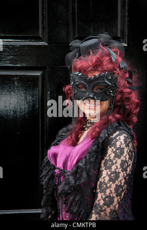 Woman. girl wearing purple goth costume with eye mask Whitby, Yorkshire, 2013. Trinity Stark, wearing fancy dress, a mask and red wig at the UK'S Biggest Goth & Alternative Weekend. Whitby. Goths, romantics and macabre fans at the Whitby Goth Weekend, which has become their spiritual home. As well as Goths, there are all manner of weird and wonderful characters with faces obscured at the Halloween Special  founded by Jo Hampshire in 1994. Stock Photo