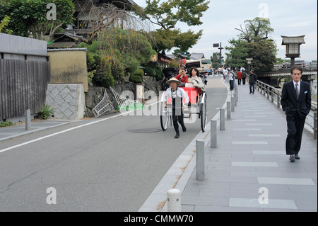 young Japanese man pulling rickshaw with two Japanese women in Arashiyama, Kyoto, Japan Stock Photo