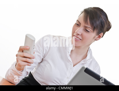 Portrait of a happy young woman looking at phone in front of a laptop computer, high key, focus on eyes Stock Photo
