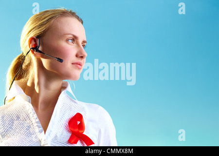 Portrait of pretty woman with headset and red ribbon on blouse over blue background Stock Photo