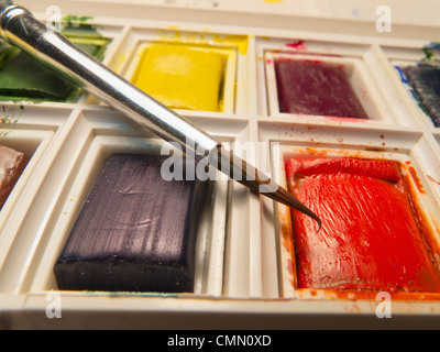 Closeup of brush poised above tablet of red water colour in a paint box. Stock Photo