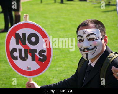 A anonymous protester wearing a mask holding a 'No Cuts' protest sign at a budget day protest in London UK Stock Photo