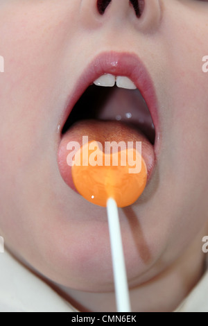 young girl licking an orange lollipop into a heart shape