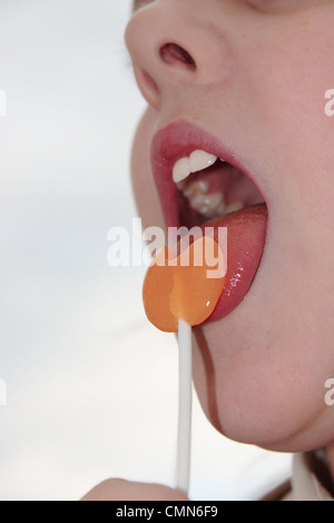 young girl licking an orange lollipop into a heart shape