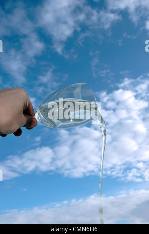 a glass of water being poured against a bright cloudy blue sky background Stock Photo
