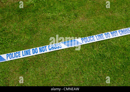 White tape with 'Police Line Do Not Cross' printed on it laying on the grass. Stock Photo