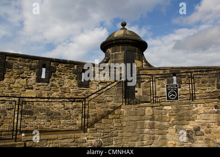 Upper section of Edinburgh Castle, with the stone wall, metal fence and a light white cloud cover over the sky Stock Photo