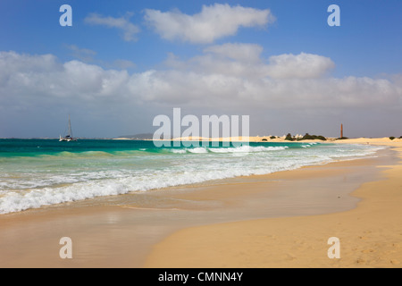 View along shoreline of quiet sandy beach with Atlantic waves and catamaran in bay. Praia de Chaves Boa Vista Cape Verde Island Stock Photo