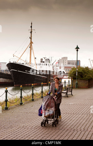 UK, England, Lincolnshire, Grimsby, Fishing Heritage Centre, woman with pram walking past Ross Tiger 1950s trawler Stock Photo