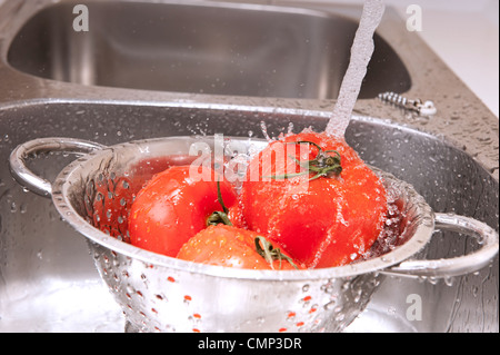 Three fresh tomatoes in colander splashing in water Stock Photo
