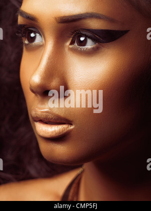 Exotic closeup beauty portrait of a young beautiful woman's face with golden skin and artistic makeup