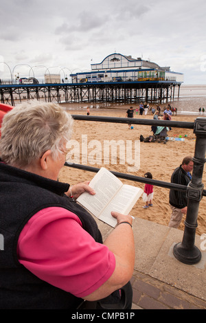 UK, England, Lincolnshire, Cleethorpes, visitor reading book on seafront beside the pier Stock Photo