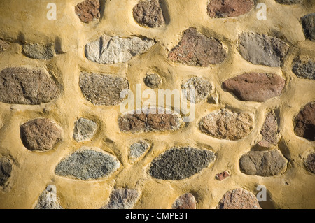 Yellow plastered wall with stones Stock Photo