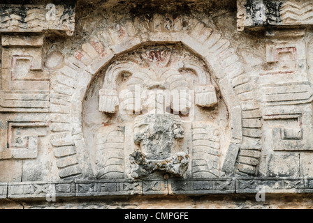 Chichen Itza Stone Relief Carving Yucatan Mexico | CHICHEN ITZA, Yucatán, Mexico — A carved figure emerges from an arched stone niche on a Maya-Toltec building at Chichén Itzá, faint traces of red pigment still clinging to its weathered border. Maya facades were once finished in vivid polychrome, a detail long since stripped away by centuries of tropical weather, leaving the bleached limestone seen by visitors today. Stock Photo