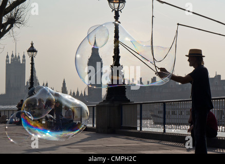 Street entertainer forming large big soap bubbles on River Thames Embankment with Houses of Parliament behind South Bank London UK Stock Photo