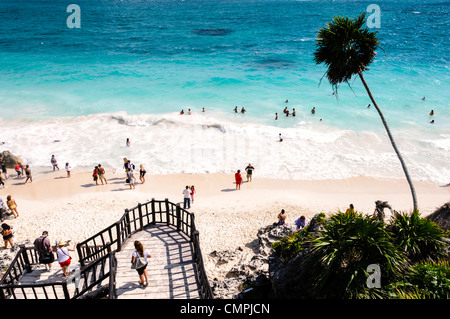 TULUM, Mexico - People swimming in the small surf of the Caribbean Sea from one of the beautiful white, sandy beaches next to the Maya civilizations ruins of Tulum on the eastern coast of Mexico's Yucatan Peninsula. In the foreground is party of the stairs from the archeological site down to the beach below. Stock Photo