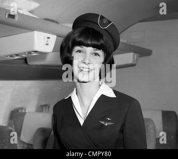 1960s SMILING PORTRAIT OF AIRLINE STEWARDESS IN AIRPLANE AISLE Stock Photo