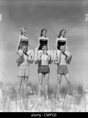 1950s COUPLES IN BATHING SUITS WALKING TOWARDS COUPLE SEATED ON SAND ...