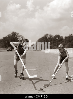 1930s 1940s 2 BOYS WITH STICKS AND PUCK WEARING ROLLER SKATES PLAYING STREET HOCKEY Stock Photo