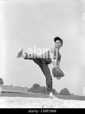 1960s BOY WEARING BASEBALL CAP TEE SHIRT BLUE JEANS AND DETERMINED EXPRESSION IN WIND-UP TO DELIVER PITCH Stock Photo