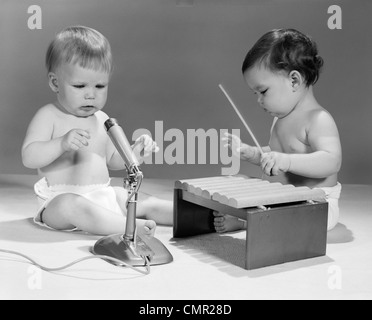 1960s TWO BABIES IN DIAPERS WITH MICROPHONE AND TOY XYLOPHONE MUSICAL INSTRUMENT PLAYING TOGETHER Stock Photo