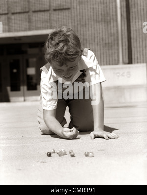 1950s SMILING BOY READY TO SHOOT KNEELING ON SCHOOL YARD GROUND PLAYING GAME OF MARBLES Stock Photo